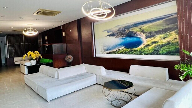 A modern living room with a large painting of a coastal landscape, white sofas, and a geometric coffee table. - Sophia Sky Hotel (Nha Trang)