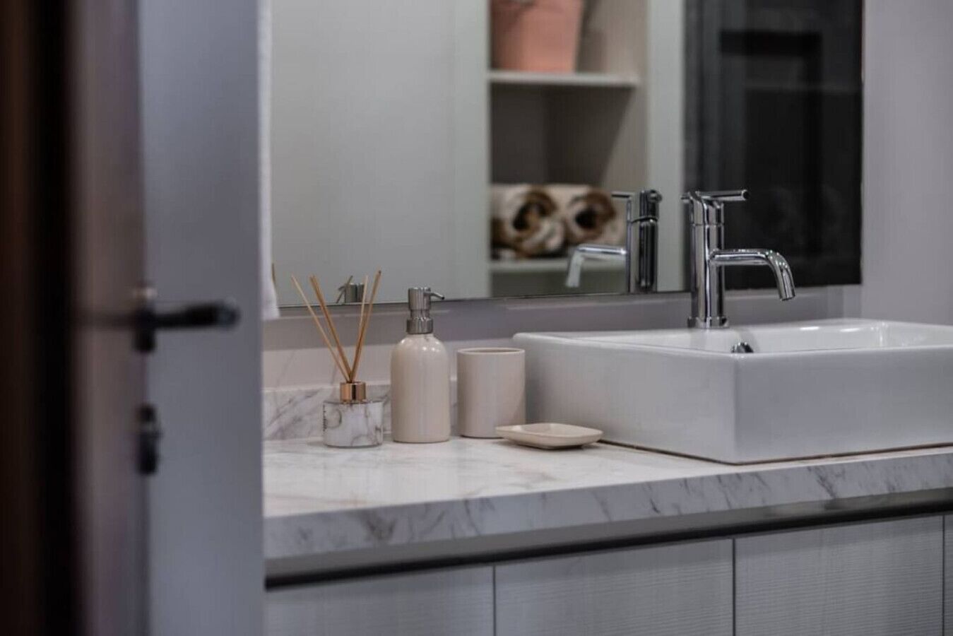 Un bagno con un lavandino bianco, uno specchio e un piano di lavoro in marmo.