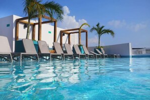 Una piscina con sillones de descanso, palmeras y una estructura de edificio moderna.
