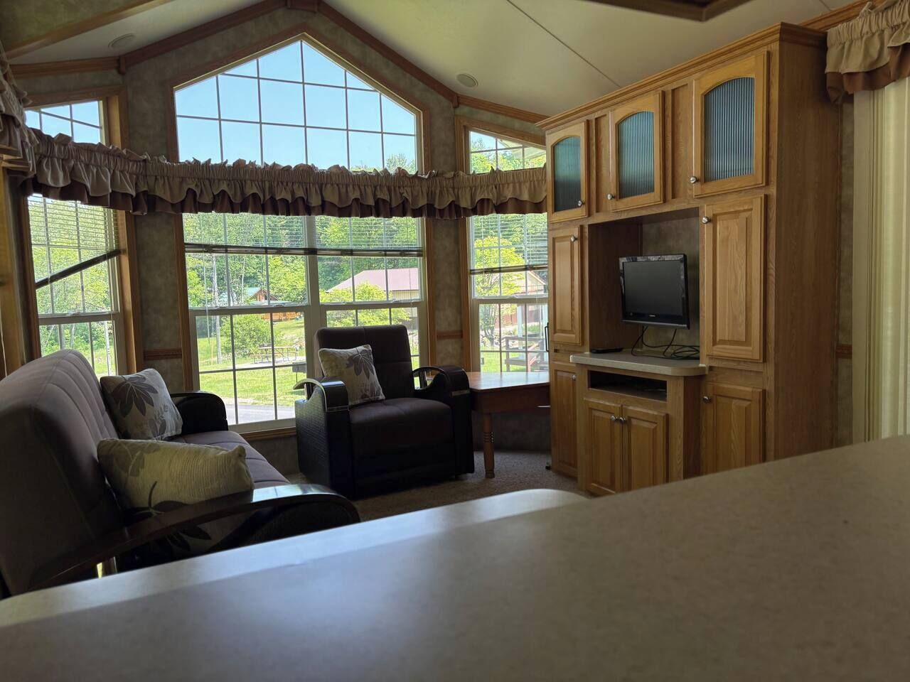 A room with a large window, a sofa, a chair, and wooden cabinets.