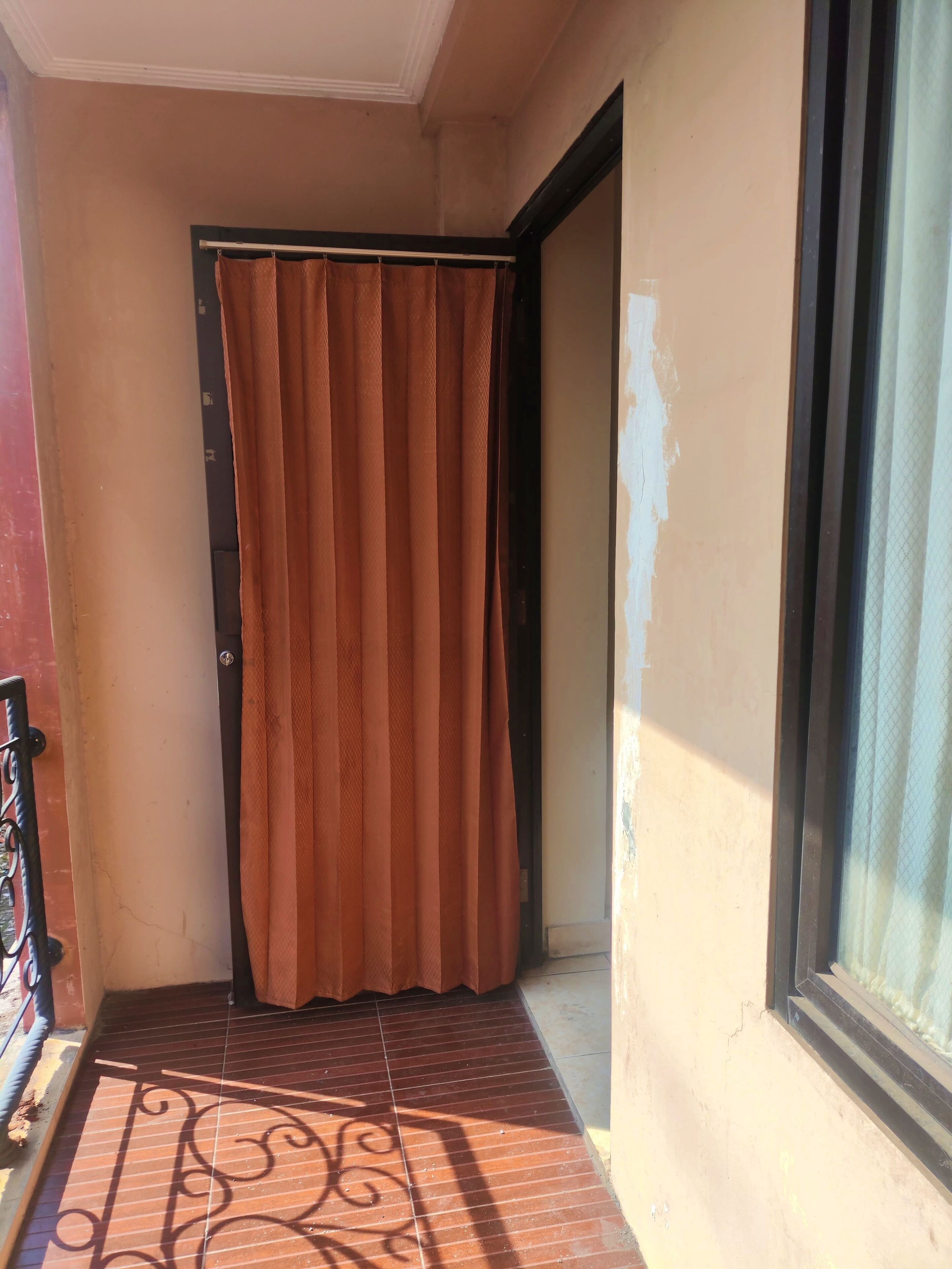 A narrow balcony with a brown curtain, a metal railing, and a tiled floor with a decorative pattern.