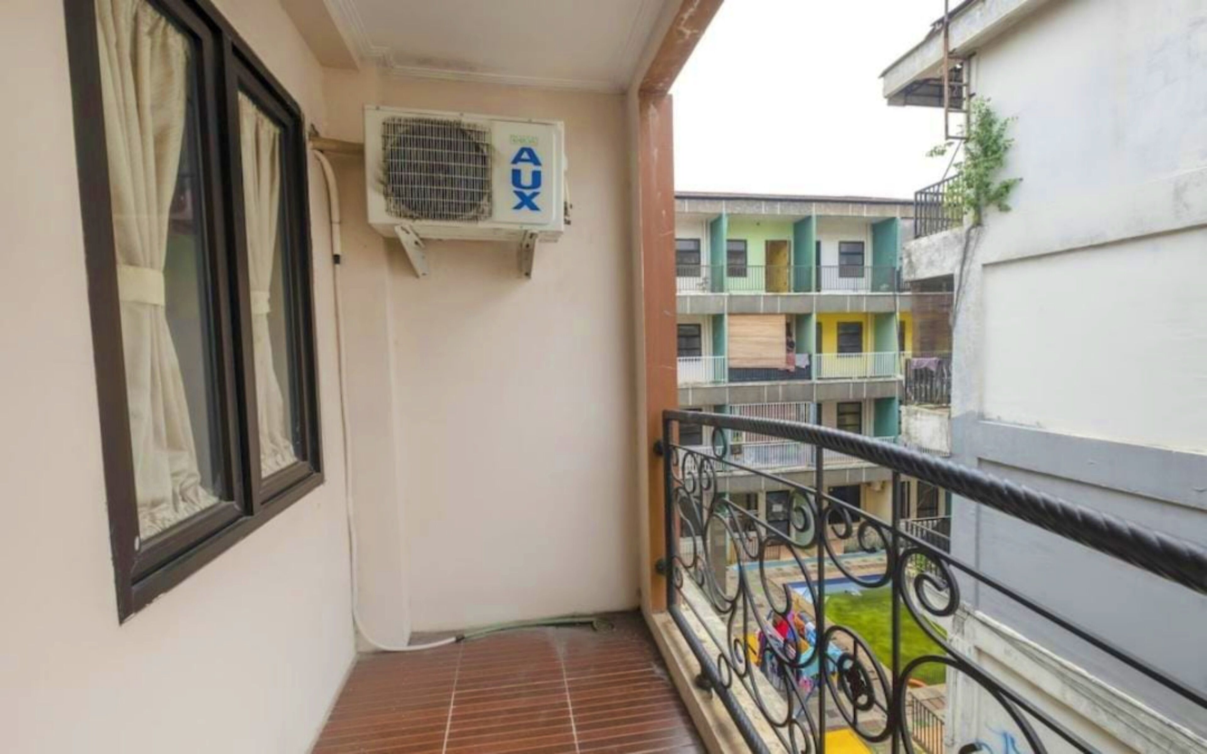 Un balcon avec une rambarde en métal, une fenêtre avec un rideau et un appareil de climatisation.