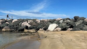 En sandstrand med stora stenar och en klarblå himmel.