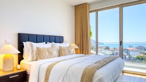 A hotel room with a large bed, two bedside tables, a nightstand, and a view of the city through large windows. - The Place Funchal View, a Home in Madeira (Funchal)