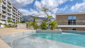 A modern hotel with a pool, palm trees, and mountains in the background. - The Place Funchal View, a Home in Madeira (Funchal)