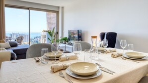 A dining area with a table set for four, a city view through large windows, and a cozy seating area with a sofa and armchair. - The Place Funchal View, a Home in Madeira (Funchal)