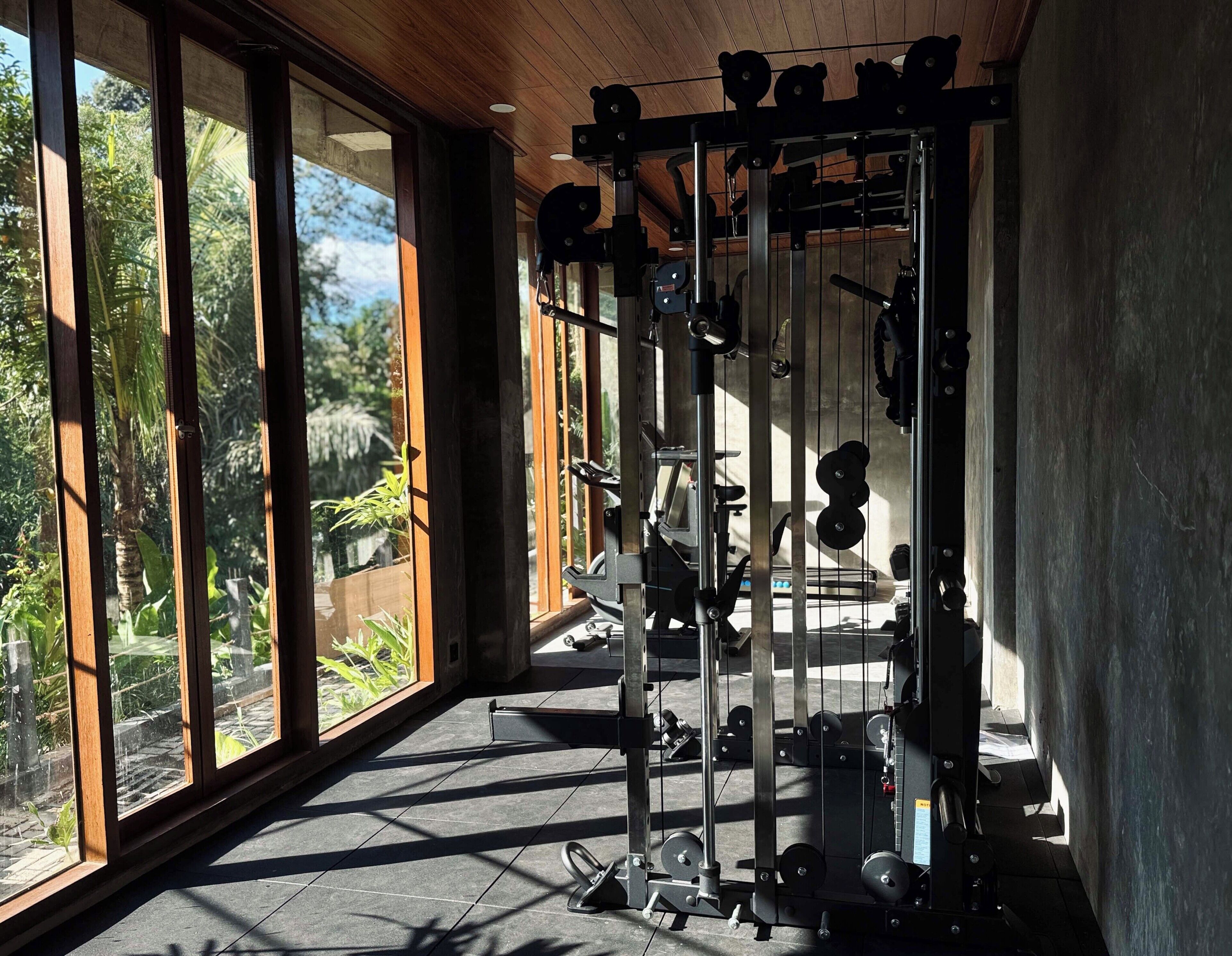 Ein Fitnessstudio mit Gewichthebereck, großen Fenstern und Blick auf Grünflächen.