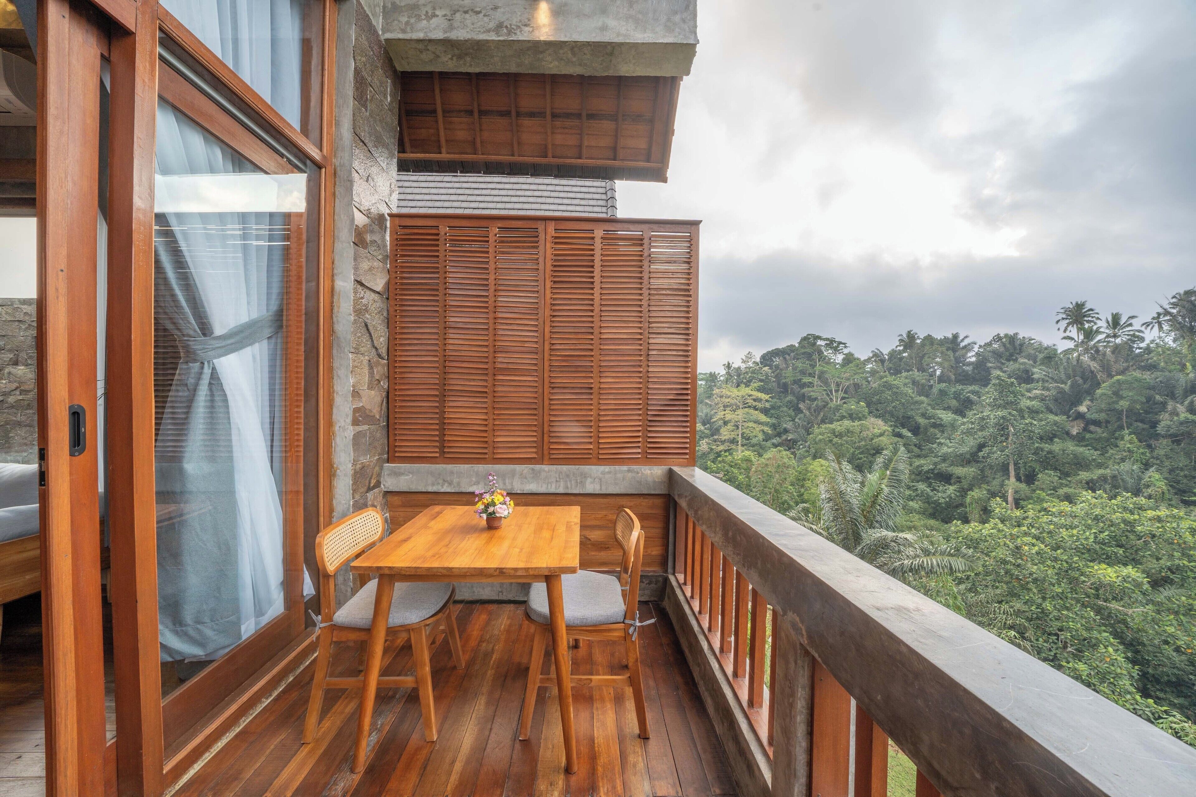 A wooden deck with a table and chairs, overlooking a lush forest.