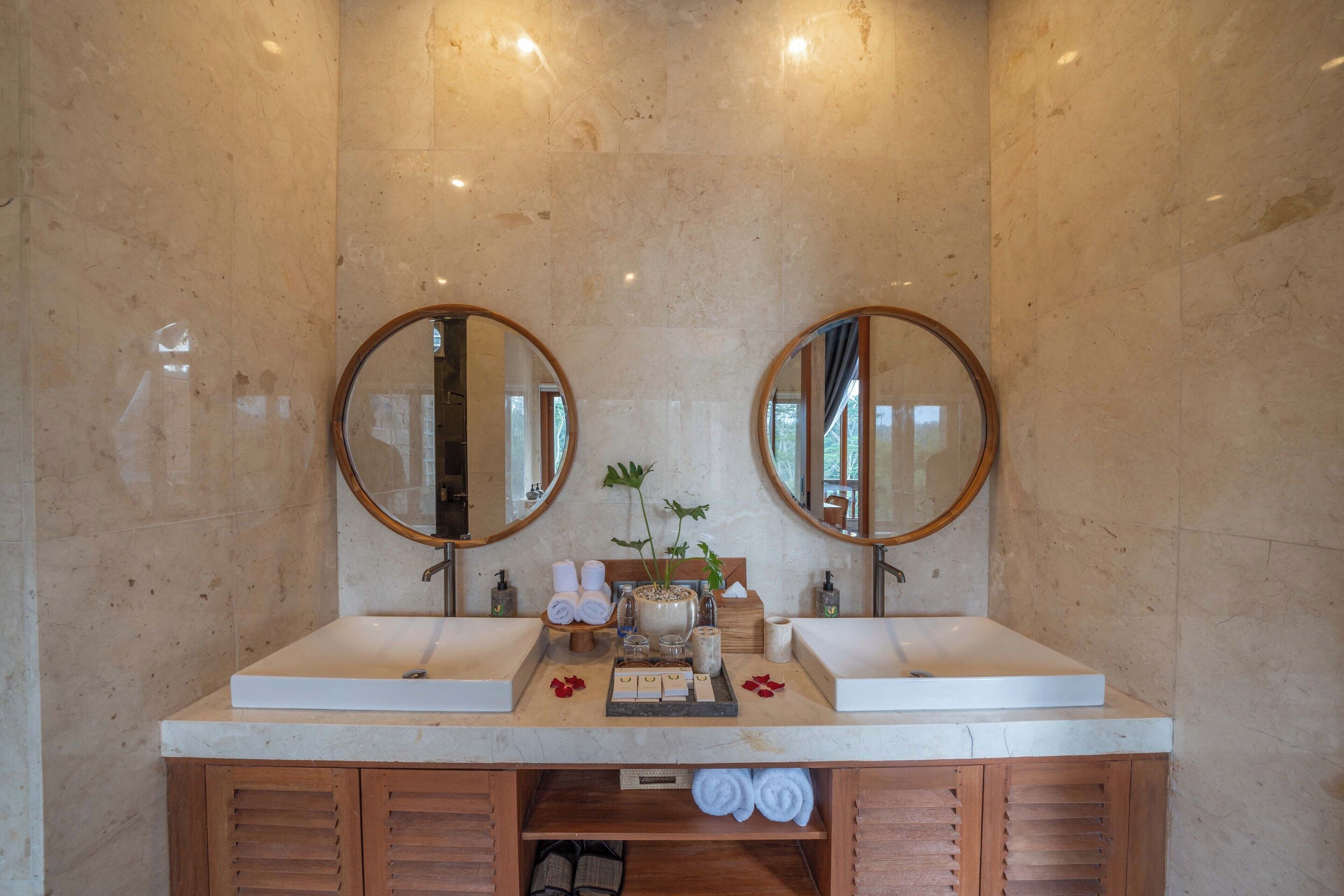 A bathroom with two sinks, marble walls, wooden cabinets, and a mirror above each sink.