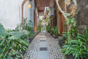 A narrow brick pathway flanked by lush greenery and stone walls, leading to a wooden door at the end. - The Lumbung Jaya Resort (Sebatu)