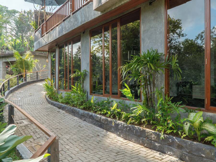 A modern building with large windows, a curved pathway, and lush greenery.