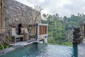 A poolside area with stone walls, lounge chairs, and a decorative stone sculpture. - The Lumbung Jaya Resort (Sebatu)