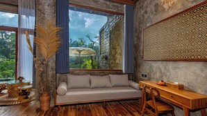 Ein Zimmer mit Holzboden, einer Couch mit Kissen, einem Esstisch mit Stühlen, einem großen Fenster mit Vorhängen und einer Wand mit Muster.