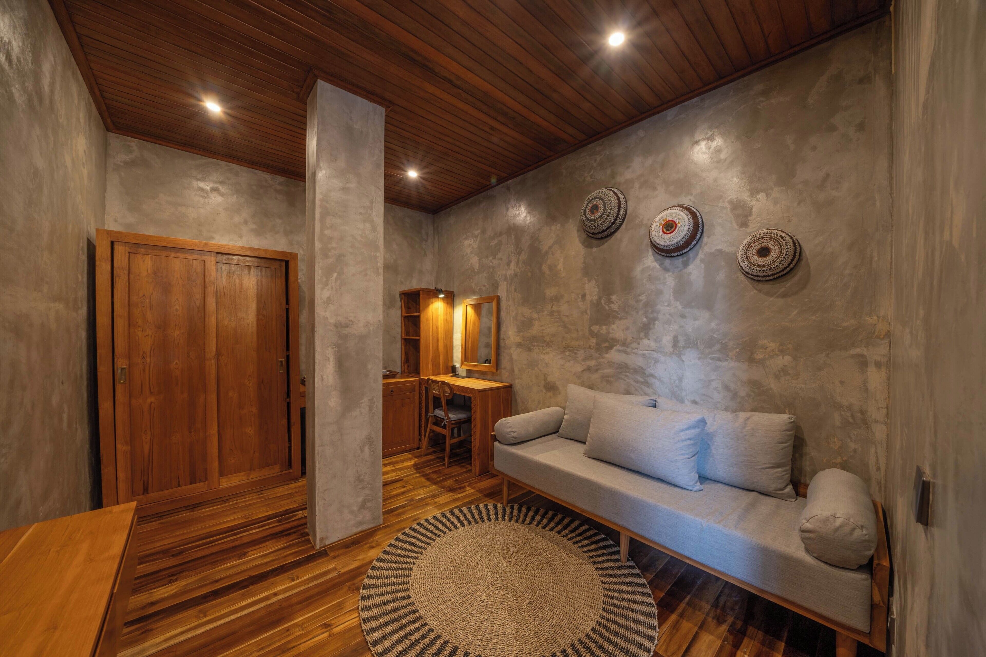 Ein gemütliches Zimmer mit Holzbalkendecke, einem Sofa, einem Schreibtisch und einem gemusterten Teppich.