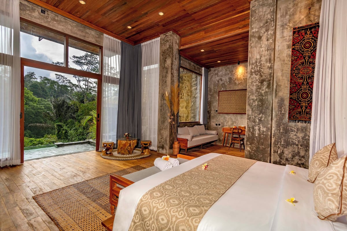 Quarto espaçoso com uma cama grande, piso de madeira e vista para vegetação exuberante.