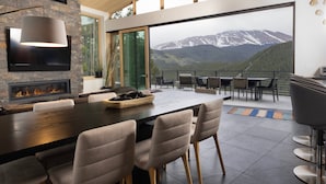 A modern dining area with a large table, comfortable chairs, a built-in fireplace, and a scenic mountain view through large windows. - Spectacular Views, Close to town, Mountain Modern elegance and entertaining! (Blue River)