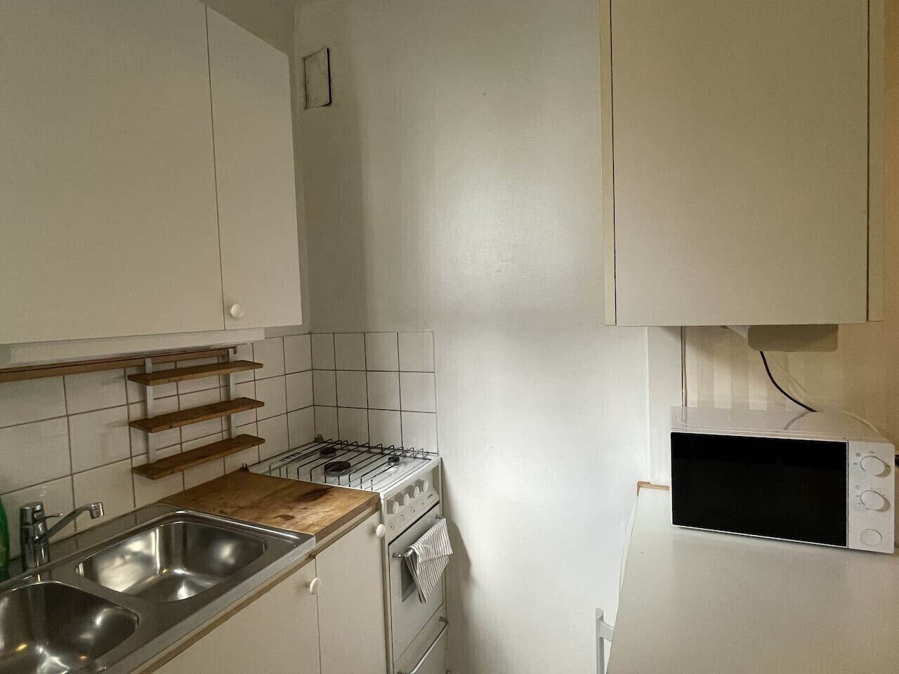 A kitchen with white cabinets, a stove, a microwave, and a wooden countertop.