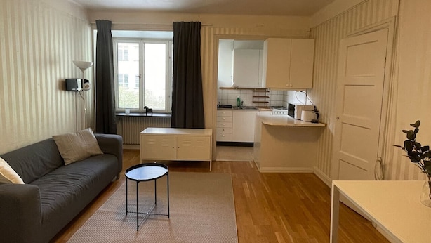 Um espaço compacto com sofá, uma pequena mesa redonda, cozinha compacta e uma porta.