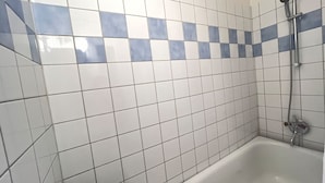 Casa de banho com azulejos brancos e azuis, uma banheira branca e um chuveiro.