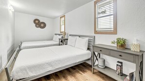 A bedroom with two beds, a bedside table with a lamp, a small potted plant, and a desk with drawers. - Family-Friendly Cottage Near Orlando’s Top Attractions (Kissimmee)