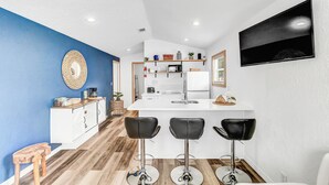 A modern kitchen with a white island, bar stools, and a flat-screen TV mounted on the wall. - Family-Friendly Cottage Near Orlando’s Top Attractions (Kissimmee)