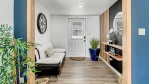 A hallway with a white door, a clock, a sofa, and a potted plant. - Family-Friendly Cottage Near Orlando’s Top Attractions (Kissimmee)