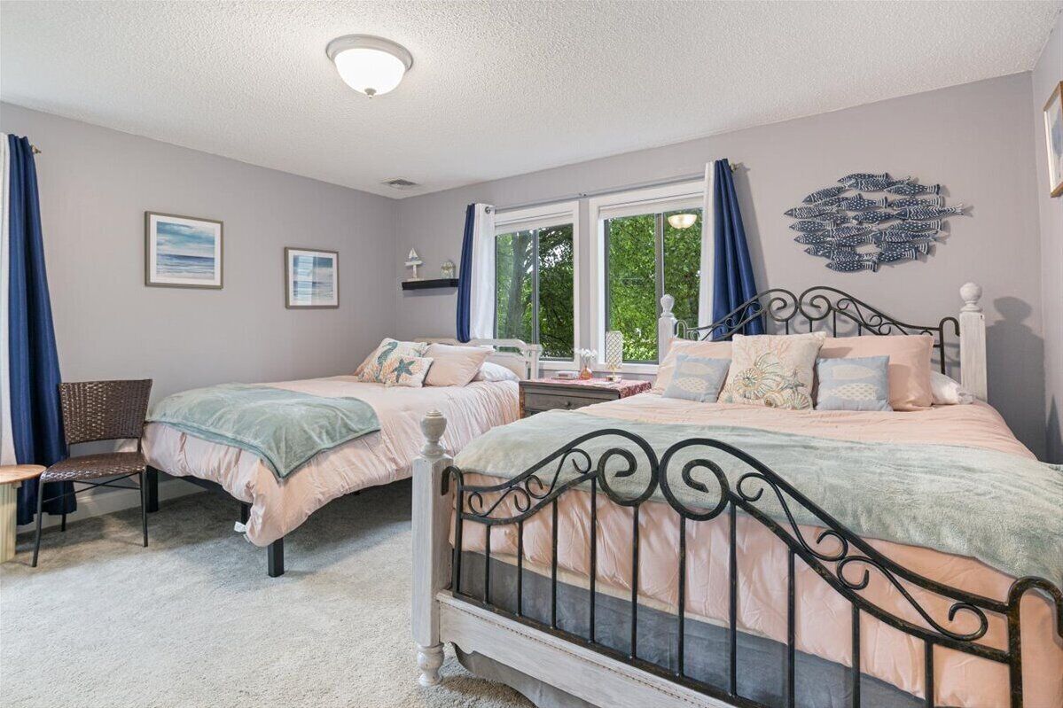 Un dormitorio con dos camas, una ventana con cortinas, una silla y decoración en la pared.