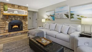 A living room with a stone fireplace, grey sofa, and artwork on the wall.