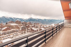 Blick vom Balkon auf eine Stadt mit schneebedeckten Häusern und Bergen im Hintergrund.