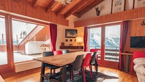 A wooden interior with a dining table, chairs, and a large window with a mountain view.