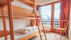 A bunk bed room with a wooden ladder, a chair, and a window with a view of snow-capped mountains.