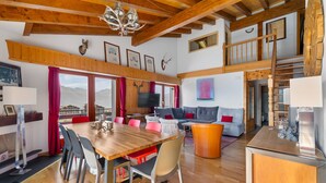 A spacious living area with a wooden dining table, red and grey chairs, a grey sofa, and a wooden staircase.