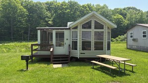 Une petite cabane à un seul étage, dotée d’un porche et d’une table de pique-nique, située dans un champ verdoyant.
