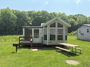 Eine kleine, eingeschossige Holzhütte mit Veranda und Picknicktisch in einer grünen Wiese.
