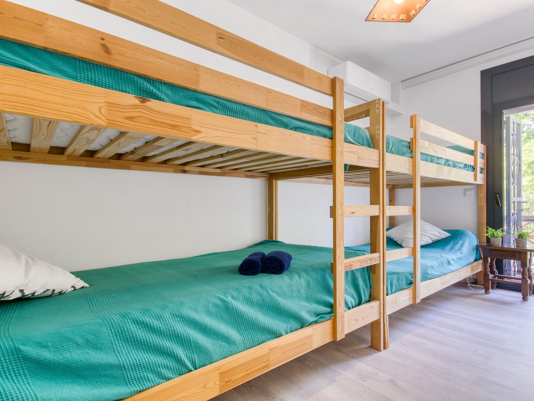 A bunk bed room with a wooden frame, green bedding, and a small table with plants.