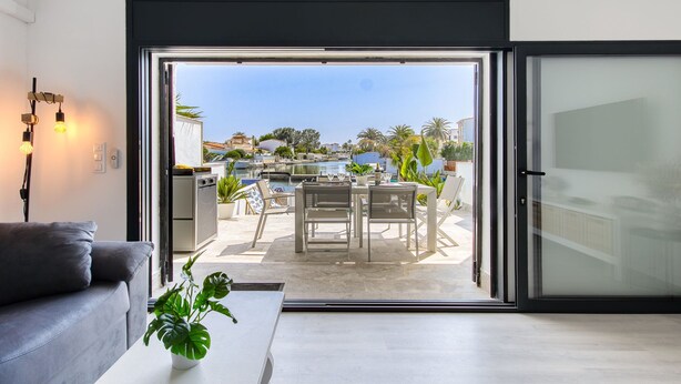 Ein modernes Wohnzimmer mit einer Schiebetür zu einer Terrasse im Freien, auf der ein Esstisch steht, mit Blick aufs Meer.