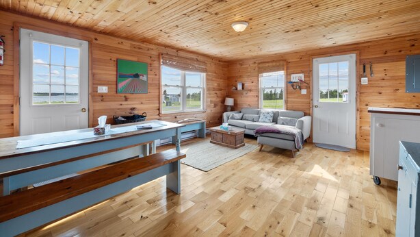 A cabin interior with a wooden ceiling, a dining area with a bench, a sofa, and a kitchen area with cabinets.