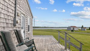 A wooden deck with a bench, overlooking a grassy area and a body of water.