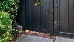 Une grille en métal noir, ornée d’une petite fenêtre et entourée de verdure.