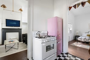 A compact kitchen with a gas stove, a pink refrigerator, and a television above the fireplace.