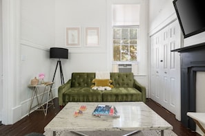 A living room with a green sofa, a coffee table, a floor lamp, and framed pictures on the wall.