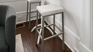 Une pièce avec une fenêtre, une table sur laquelle se trouvent une bouteille et des verres, et deux tabourets.