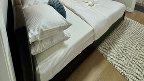 A double bed with white linens and a dark headboard, a bedside lamp, a window with blinds, and a small rug on the floor.