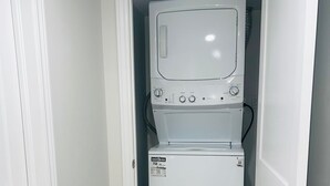 A laundry room with a stacked washer and dryer, wooden flooring, and a black rug.