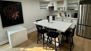 A modern kitchen with white cabinetry, a stainless steel refrigerator, and a dining area with a white table and black chairs.