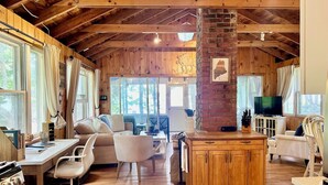 A cozy cabin interior with a wooden ceiling, a brick fireplace, a dining area, and a TV. - Seaside Cabin Retreat – Breathtaking Views & Ocean Access (Harpswell)