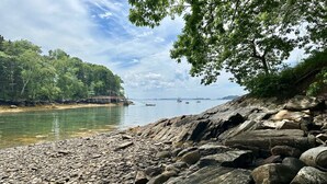 A rocky shoreline with a wooden pier extending into calm waters, surrounded by dense greenery. - Seaside Cabin Retreat – Breathtaking Views & Ocean Access (Harpswell)