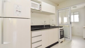 Une cuisine moderne avec des meubles blancs, un four à micro-ondes encastré, une cuisinière à gaz et un évier.