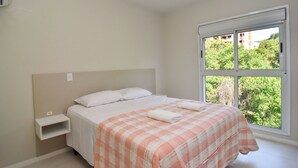 Une chambre à coucher avec un lit, une table de chevet, une fenêtre donnant sur un paysage verdoyant et un mur blanc.