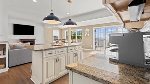 Cocina moderna con muebles blancos, encimeras de granito e iluminación colgante.